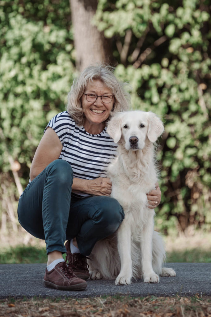 Ein Portrait der Hundetrainerin Barbara, wie sie neben ihrem Hund in die Hocke geht.