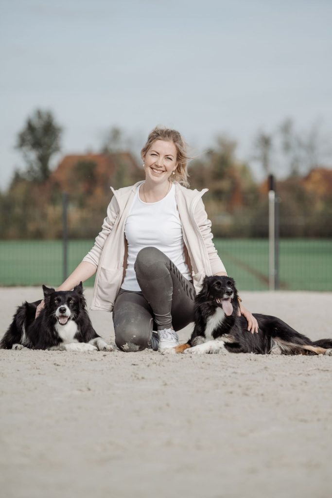 Ein Portrait der Hundetrainerin Lea wie sie zwischen ihren beiden Border Collies kniet.