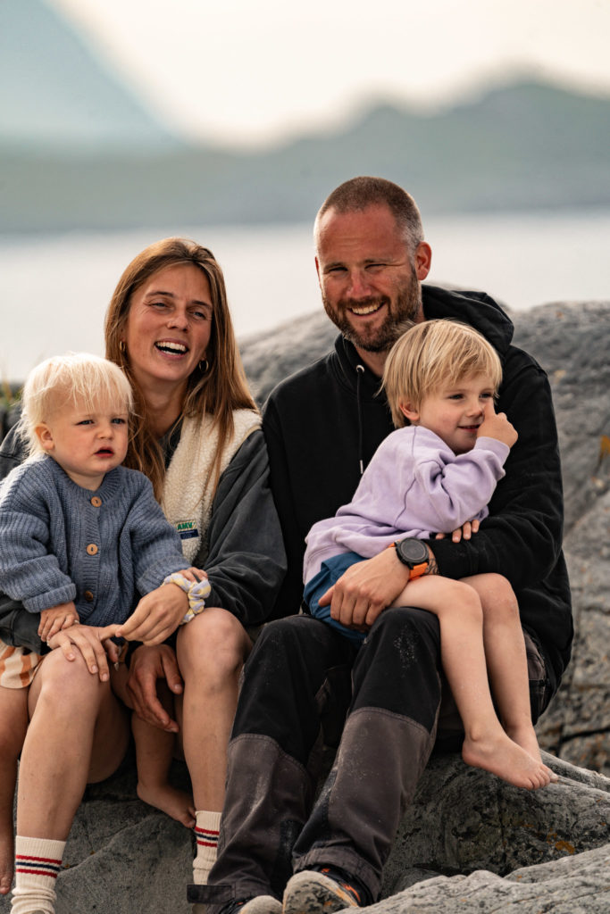 Florian Symanzig mit seiner Familie am lachen. Neben ihm sitzt seine Frau Pia und beide haben jeweils eines ihrer Kinder auf dem Schoß.