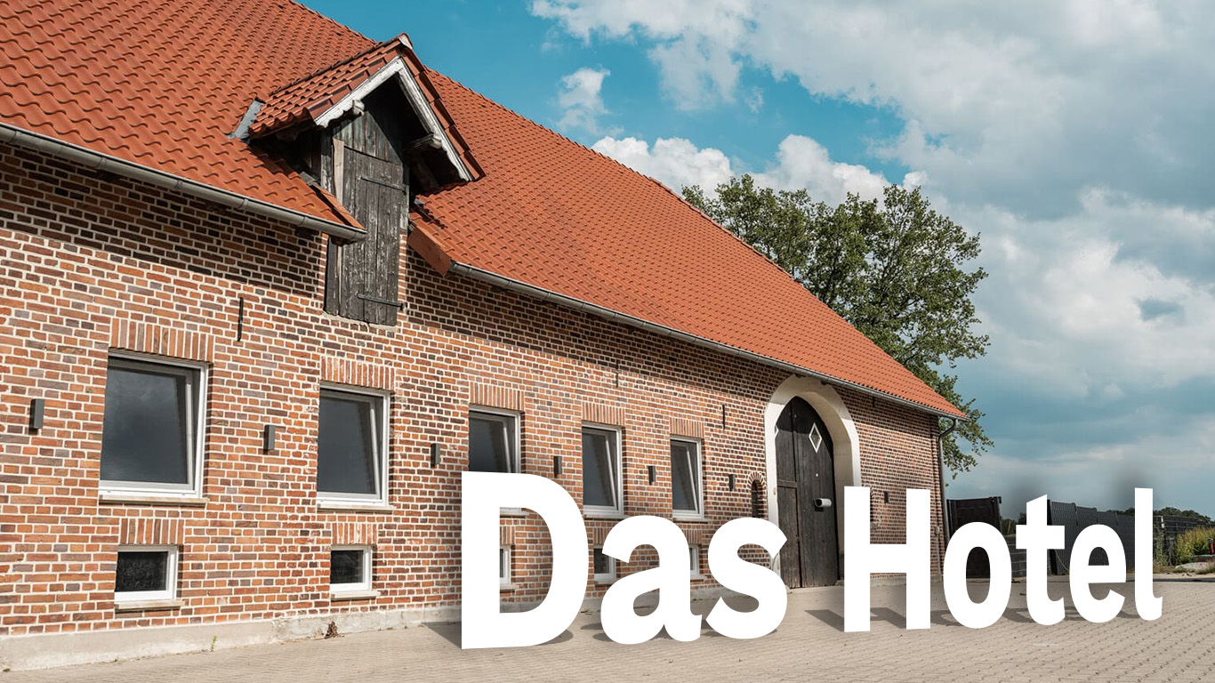 Frontansicht des Hundehotels der Komm! Hundeschule in Senden. Backsteinhaus mit bodentiefen Fenstern und Scheunentor. Im Vordergrund ist der Schriftzug "Das Hotel"