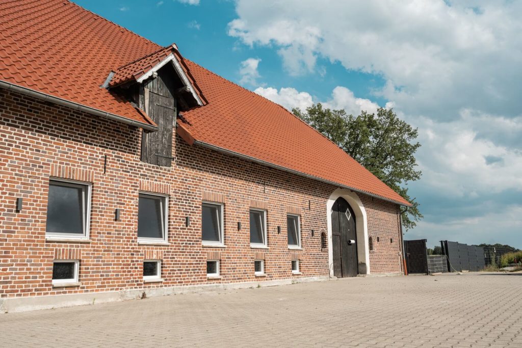 Frontansicht des Hundehotels der Komm! Hundeschule in Senden. Backsteinhaus mit bodentiefen Fenstern und Scheunentor