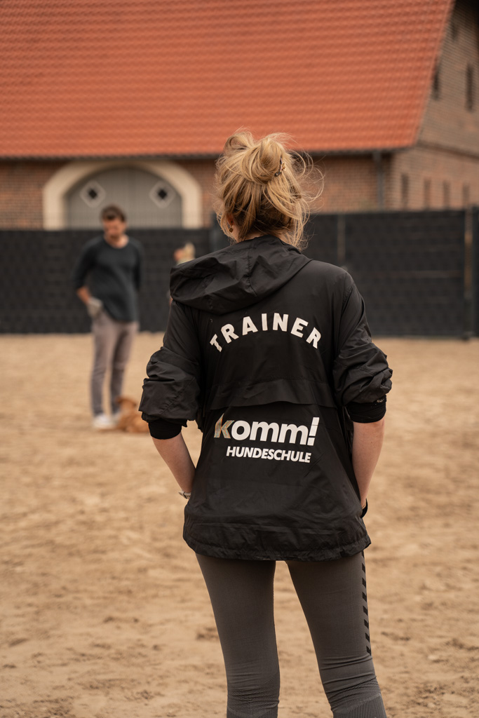Trainerin der komm! Hundeschule steht auf dem Hundeplatz und leitet den Junghundekurs