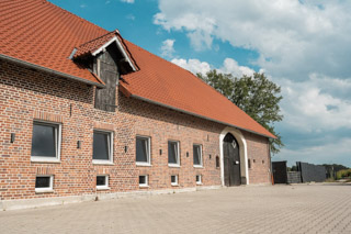 Frontansicht des Hundehotels der Komm! Hundeschule in Senden. Backsteinhaus mit bodentiefen Fenstern und Scheunentor